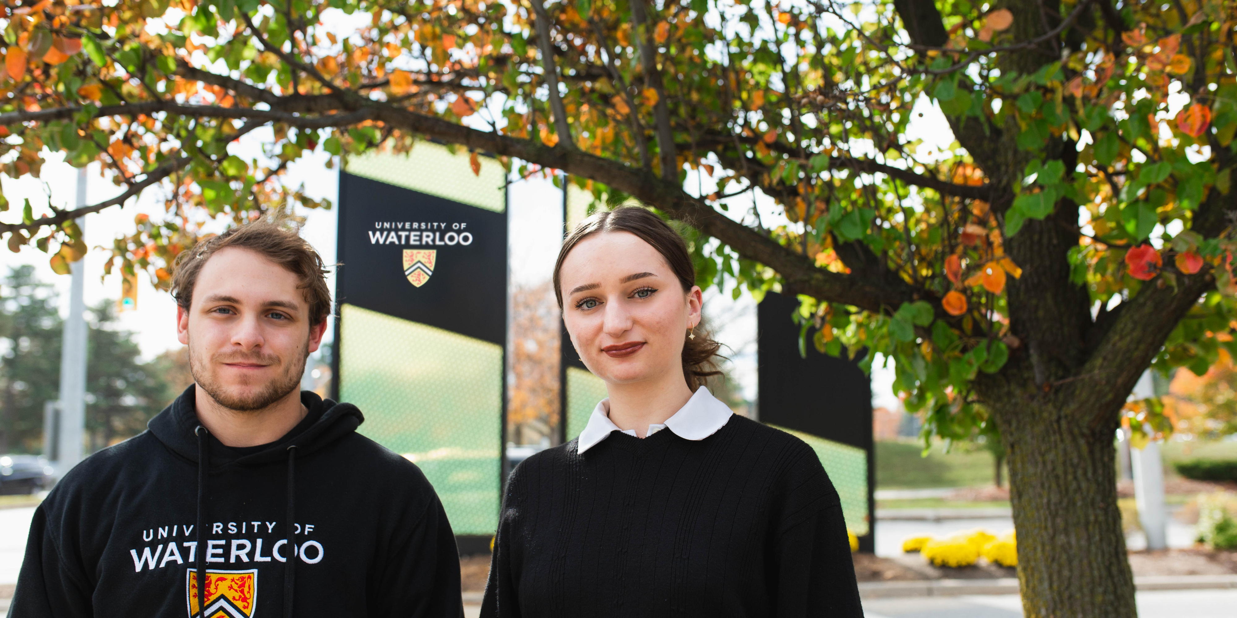 man and woman standing in front of university of waterloo sign