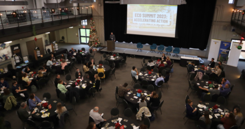 People sitting in a room in front of a screen that says Eco Summit 2023