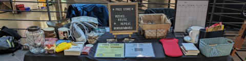 A table with household items placed on it. A sign reads, "Free Store. Reduce, Reuse, Repeat. @uwsustainable".