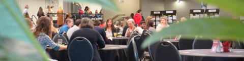 Employees eating lunch at Eco Summit in background, plant leaves in foreground