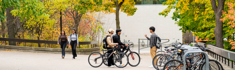 Students on bicycles across from EV1, with fall foliage in the background