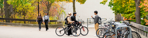 Students on bicycles across from EV1, with fall foliage in the background