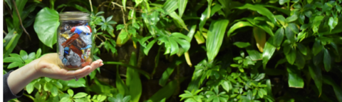 A mason jar of trash in front of a living plant wall