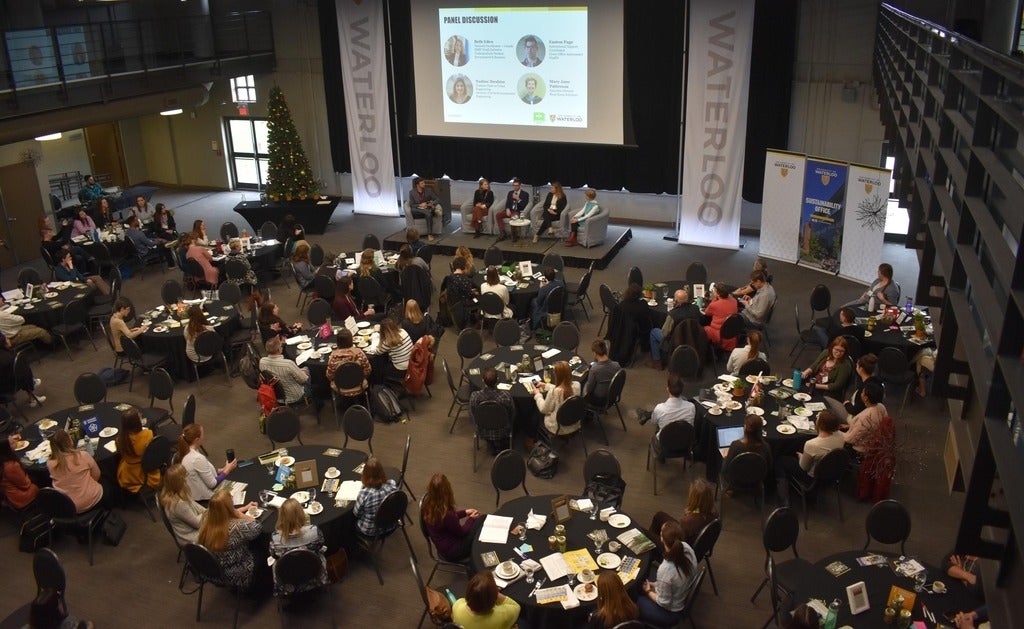 Aerial shot of Eco Summit event, with panel members on stage and participants at round tables in audience