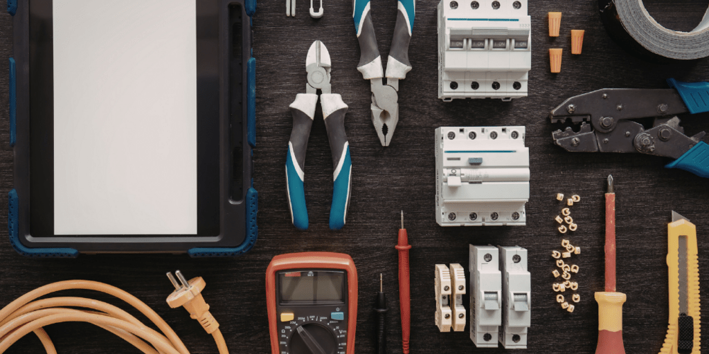 Assorted repair tools (screwdriver, nails, razor knife, pliers) on black tablecloth