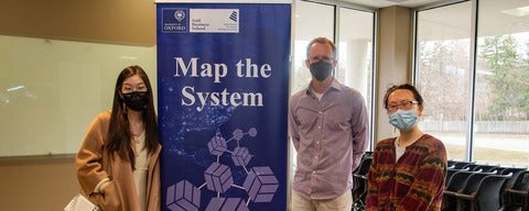 Three people standing by Map the System banner