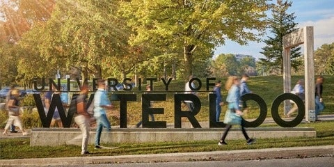 Students walking in front of University of Waterloo sign at entrance of school