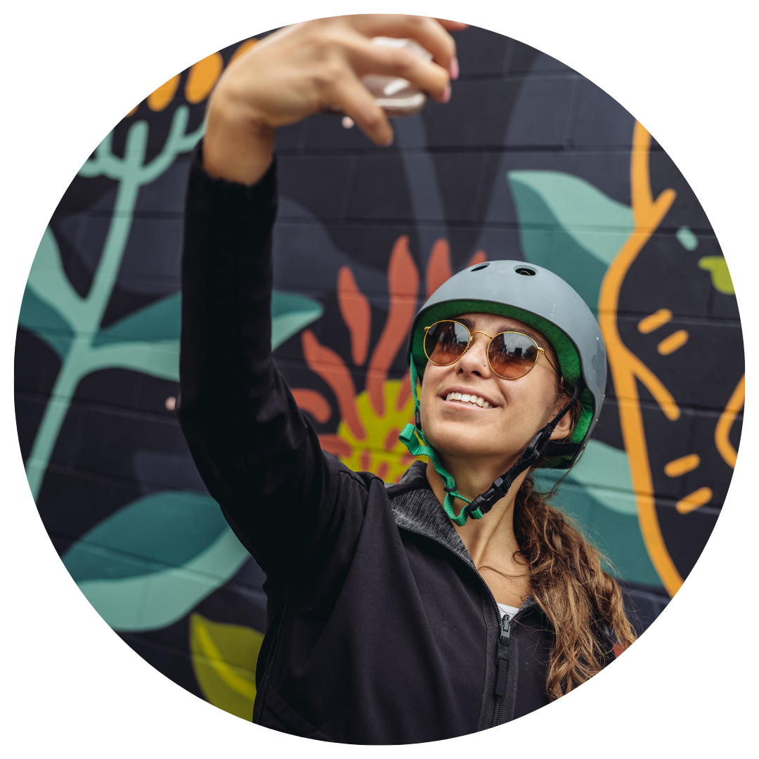 Woman standing in front of a colourful mural taking a selfie with a bike helmet on