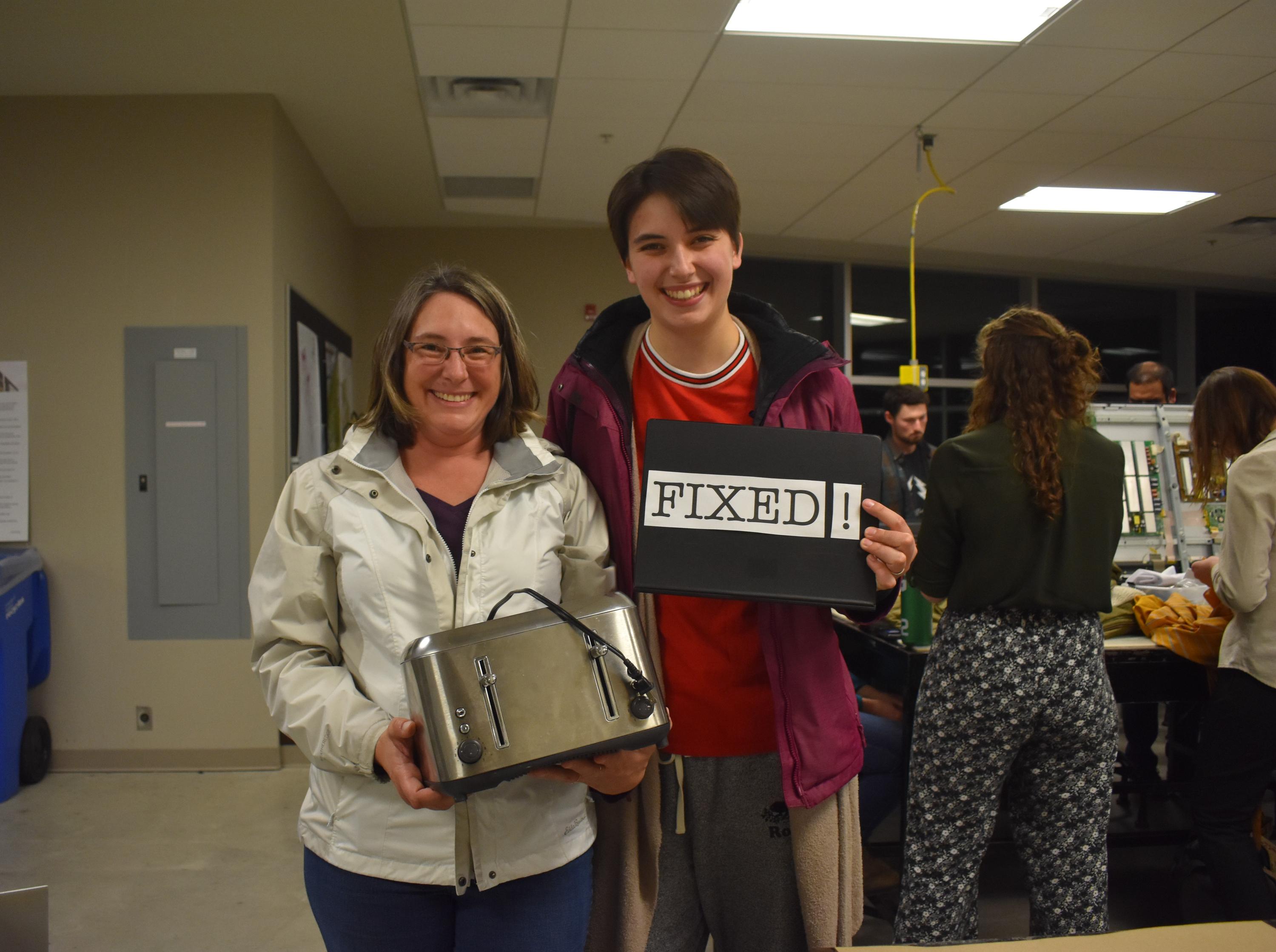 Mother and daughter posing with "FIXED" sign and fixed toaster