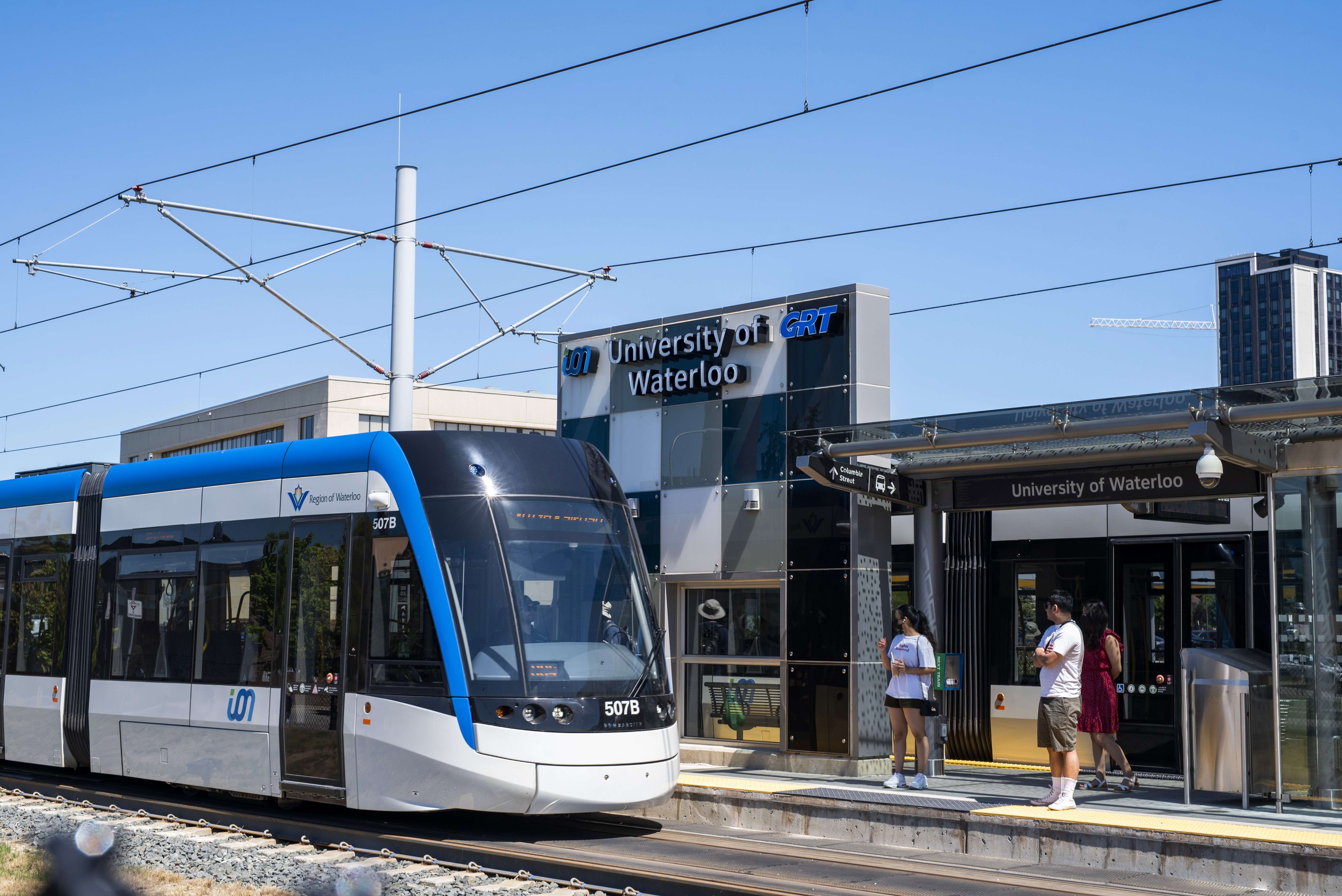 A light rail train is pulled up to UW station and two students prepare to board.