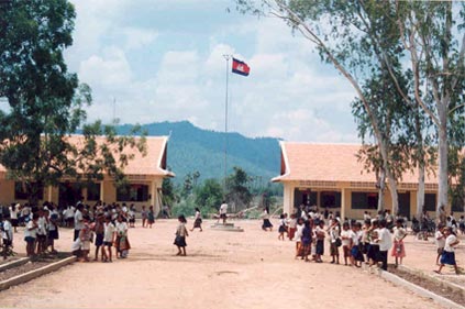 two buildings filled with people in a rural Cambodia with a single flag between them