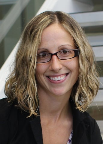 Image of a person with shoulder-length blonde hair and glasses, smiling and wearing a black top