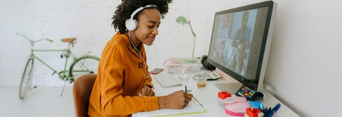 woman sitting at desk looking down at school work with computer desk top in front of her. 