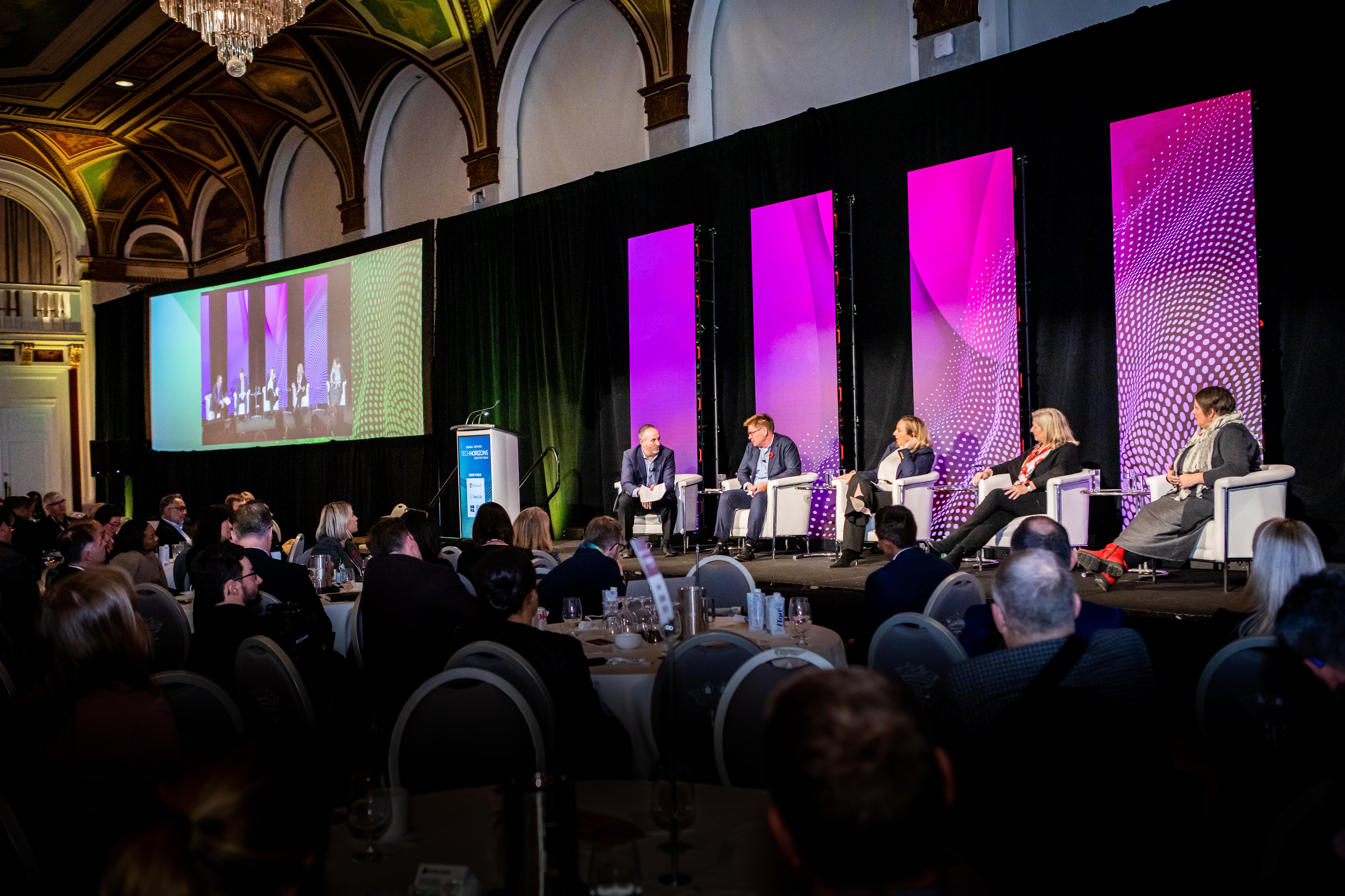 Audience listening to five speakers on stage in panel discussion