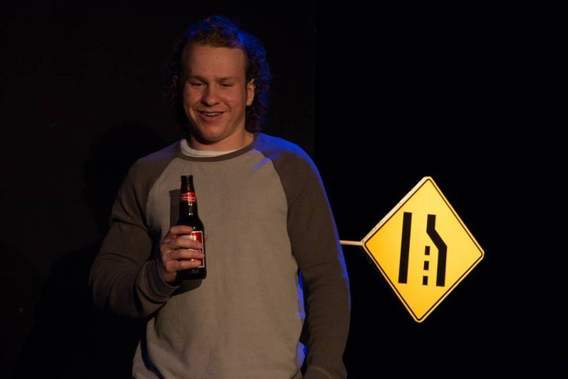 Man holds beer bottle with road sign behind him