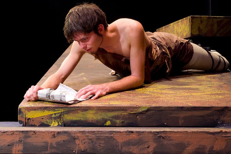 Man laying down and reading a scroll in the play 'Julius Caesar