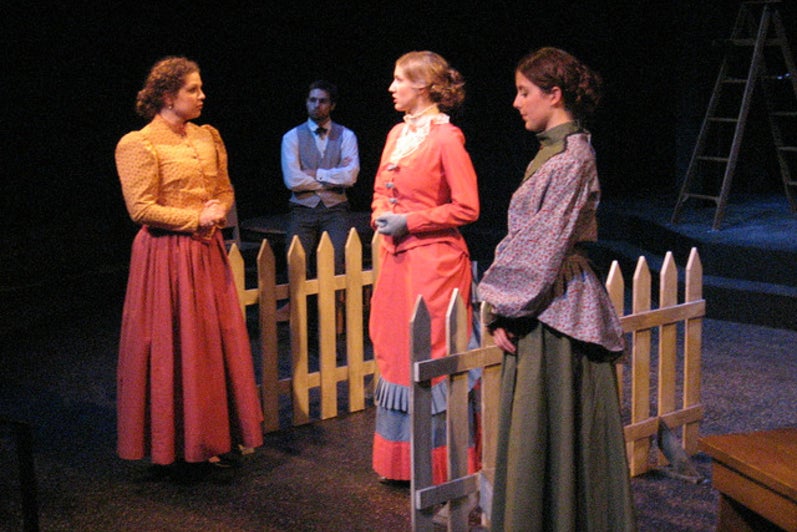 Three women in dresses talking with a man sitting in the background