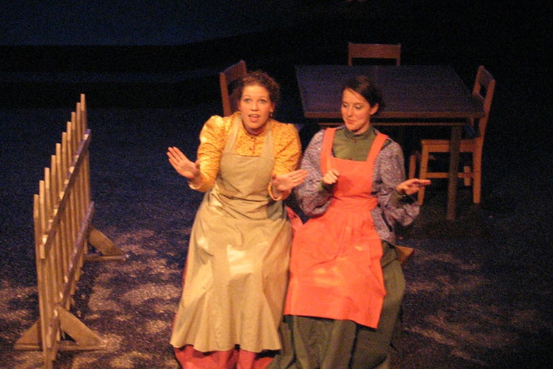 Two women sitting on stage in dresses