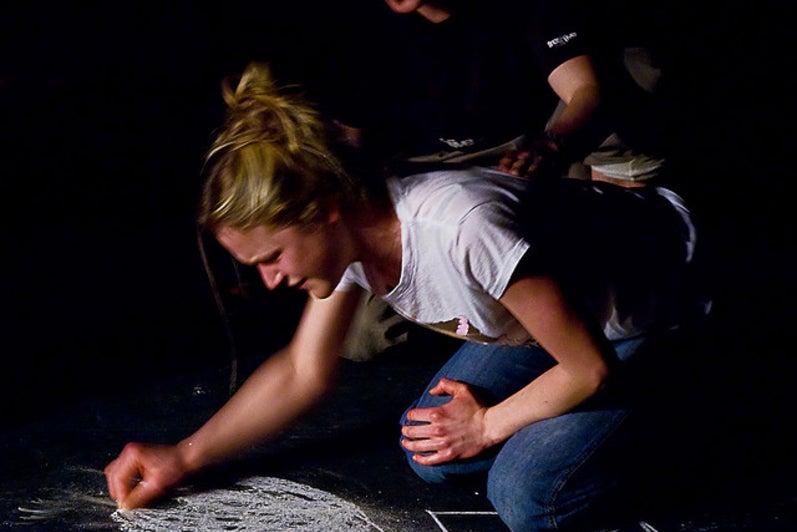 Girl drawing on ground with chalk with a man kneeling behind her