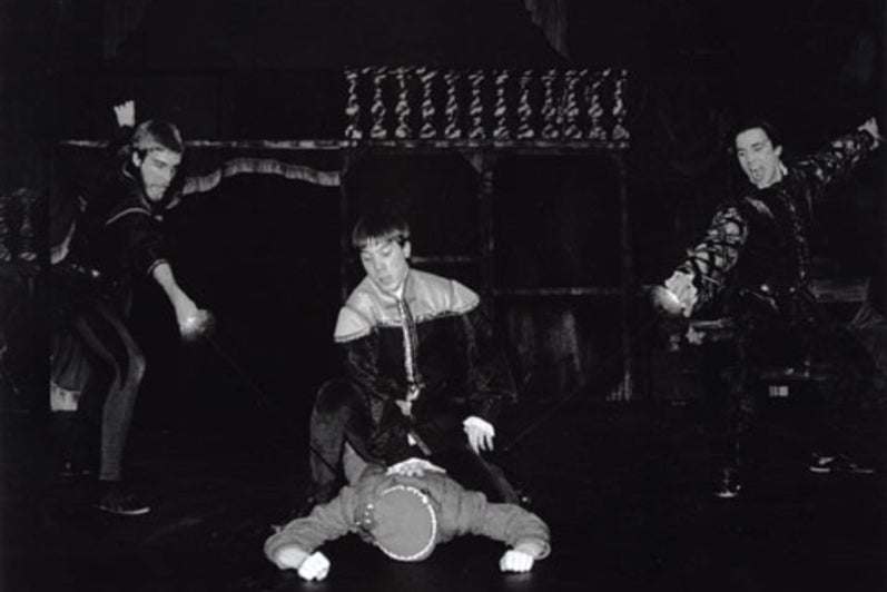 Man holding down another person with two people pointing swords in the background