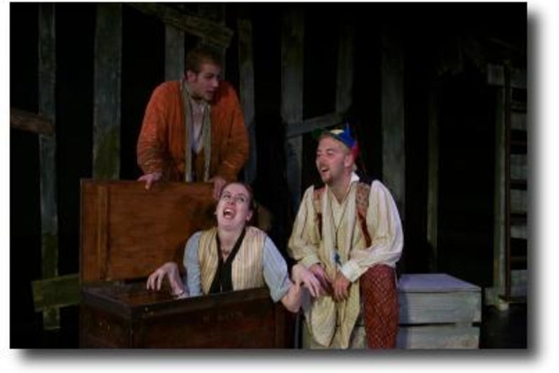 A woman being revealed from a box with two men looking on by her side