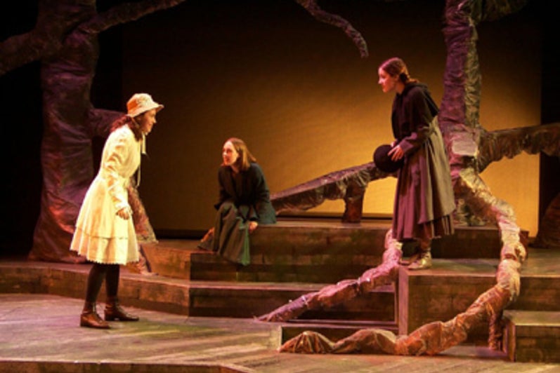 Three women walking to each other on a forest-themed stage