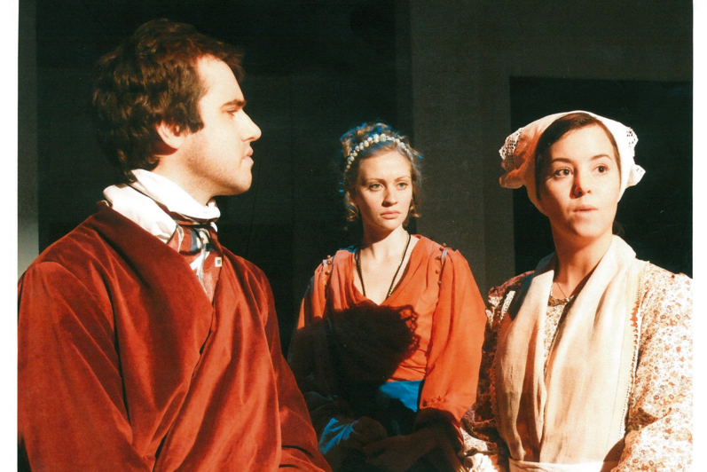 One man in red cloak and two women looking off-screen