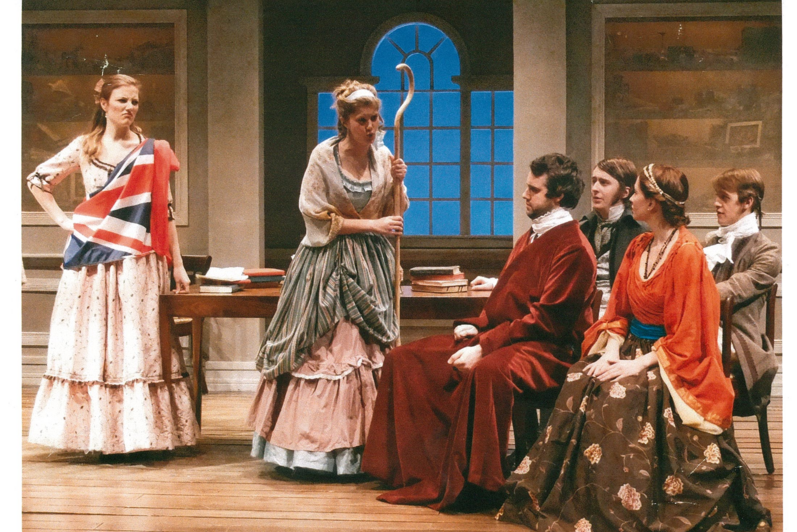 Four people sitting looking at two women standing to the left