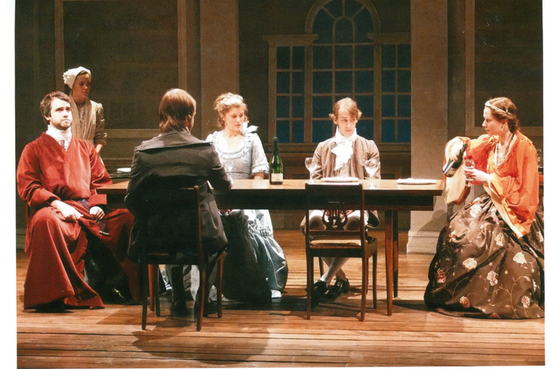Five people sitting at a dinner table and a maid standing to the side