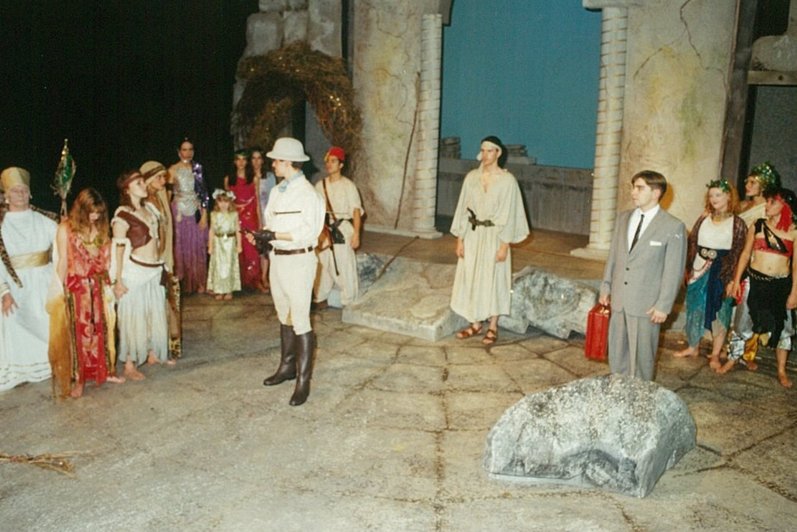 A group of people in colourful loose clothing surrounding a man in a European explorer outfit