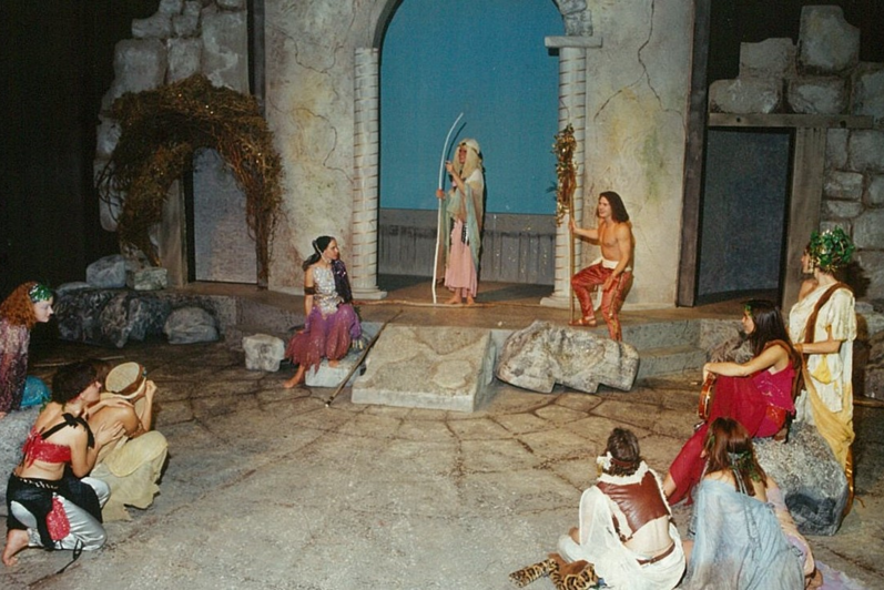 A group of people in colourful clothing gathered around a man with a white wooden staff