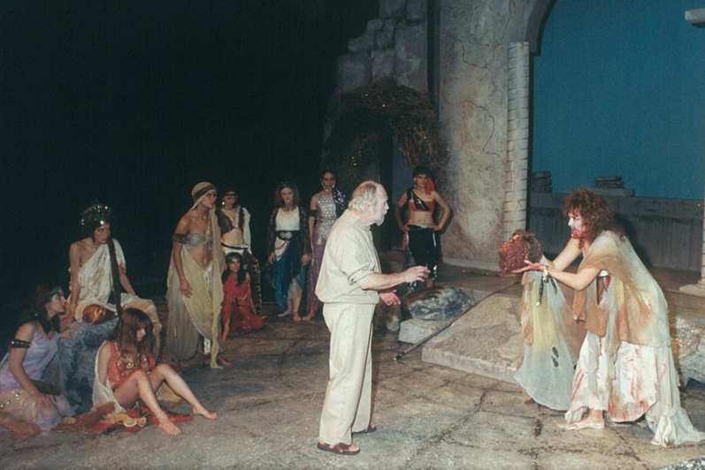 A man showing head to another man in modern clothing, a group of people surround them