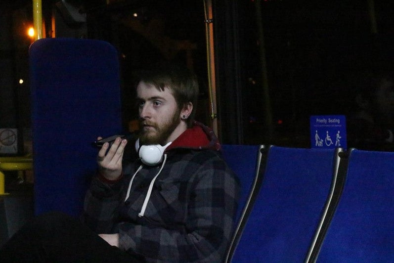 Man sits on bus, talking into a walkie-talkie