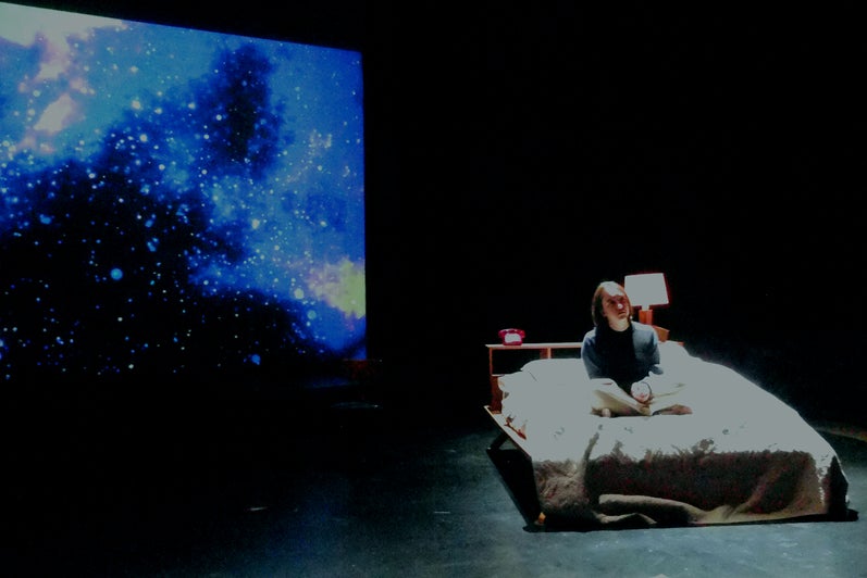 A bed is on stage and stars are projected behind