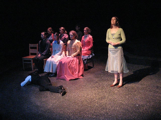 Group of people sitting on stage with a man lying face down on the ground in front of them