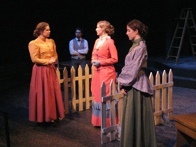 Three women in dresses talking with a man sitting in the background