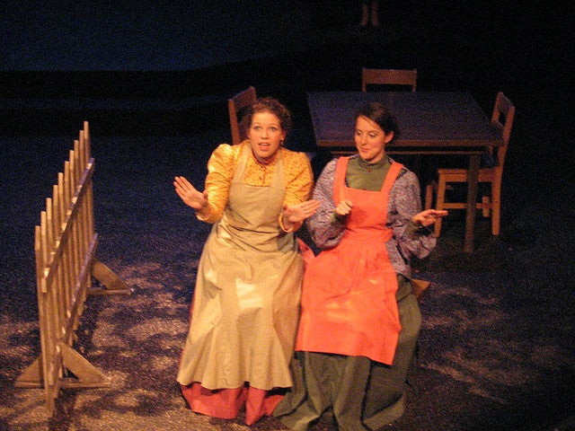 Two women sitting on stage in dresses