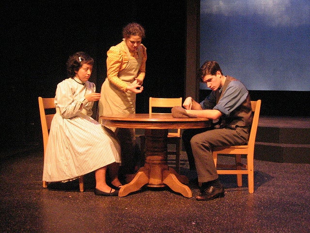 Man and a woman sitting at a table while another woman speaks to them