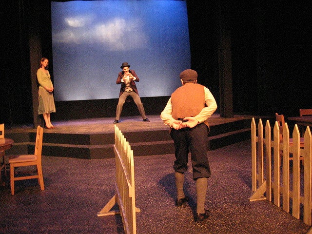 Two men face-off on stage while a woman looks on