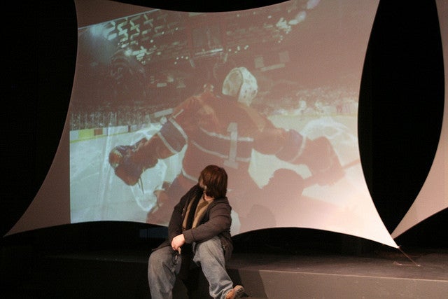 Boy sitting with hockey on screen behind him