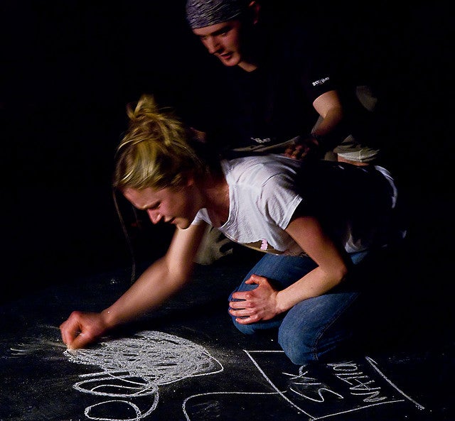 Girl drawing on ground with chalk with a man kneeling behind her