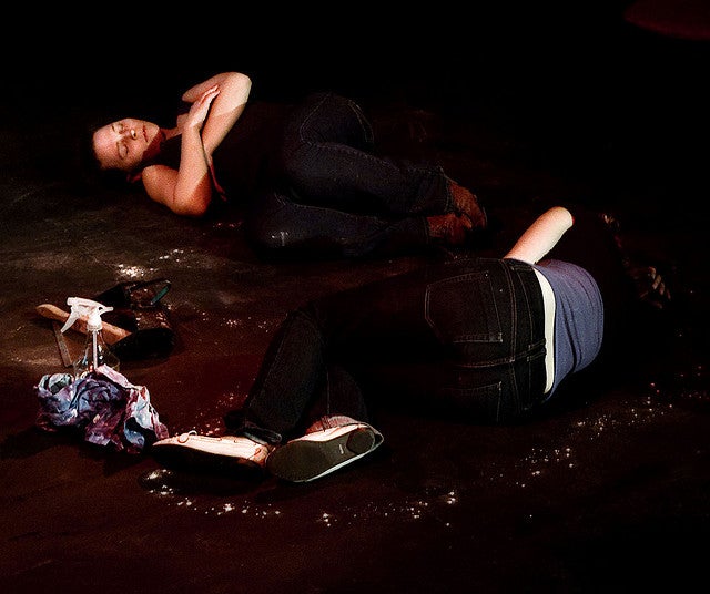Two people on the ground pretending to be dead in the play Differ/End: The Caledonia Project