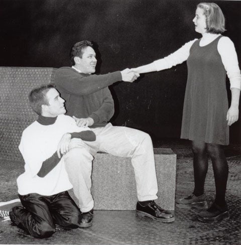 Man shaking the hand of a woman while another man looks on from his knees