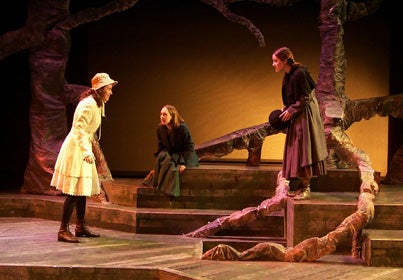 Three women walking to each other on a forest-themed stage