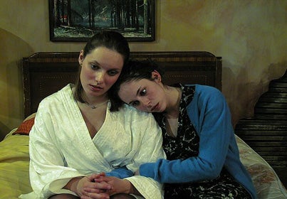 Two women sitting on a bed with one's head on the other's shoulder