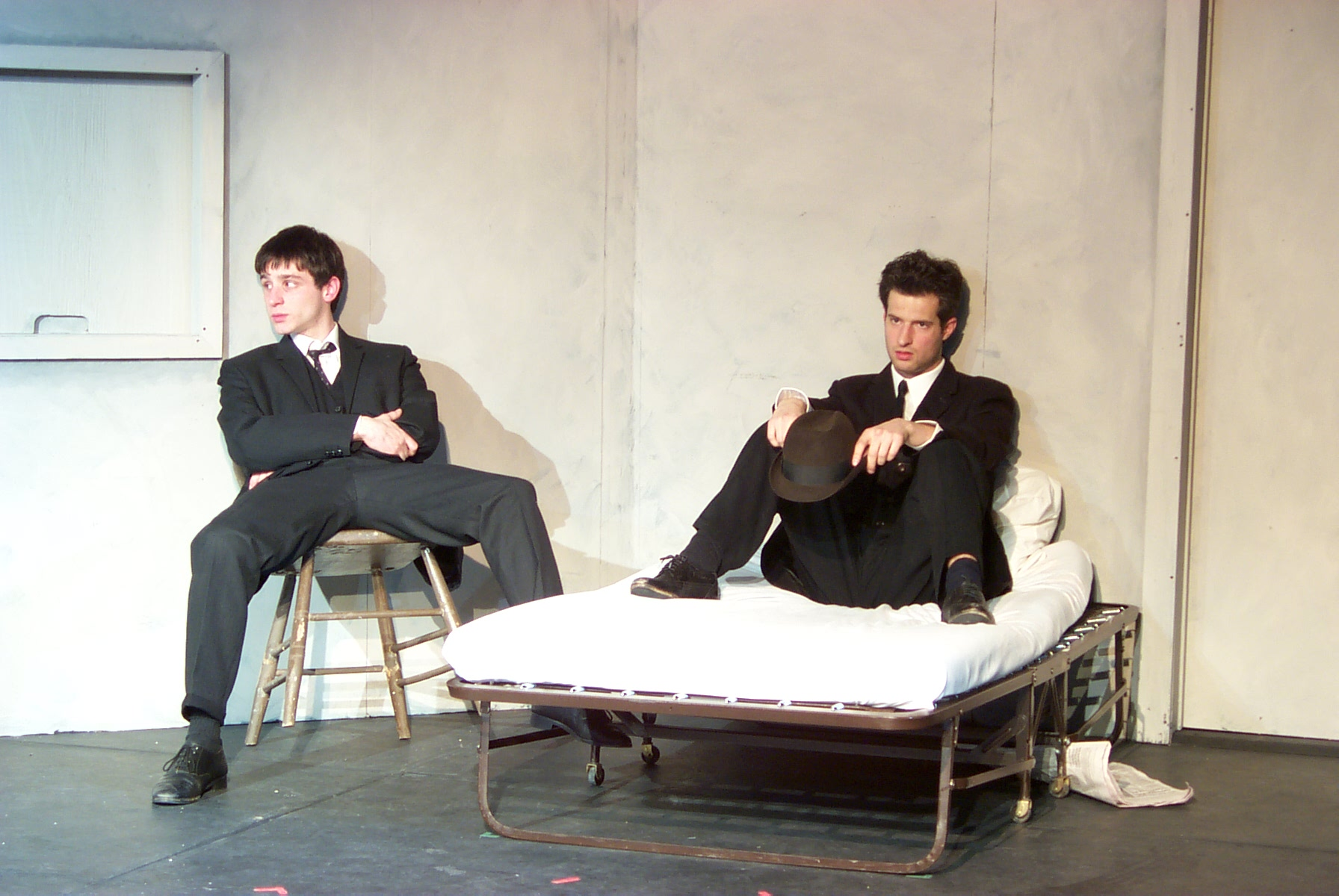 One man sitting on a chair and another man sitting on the bed