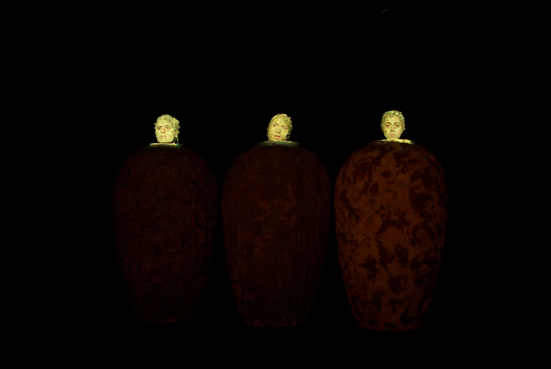 Three people enclosed in big vases, their heads lit up by a spotlight