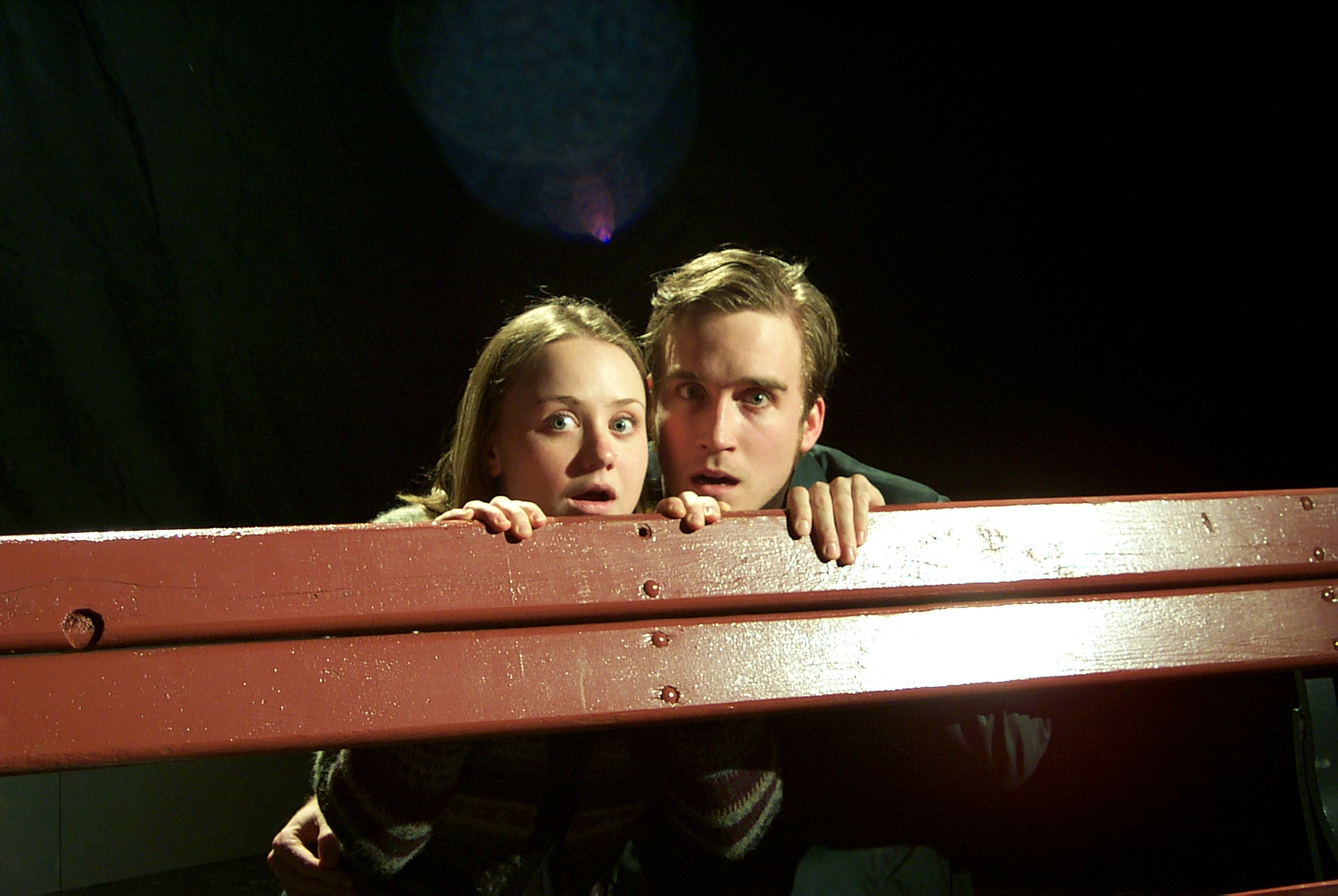 A woman and a man peeking behind a wooden bench