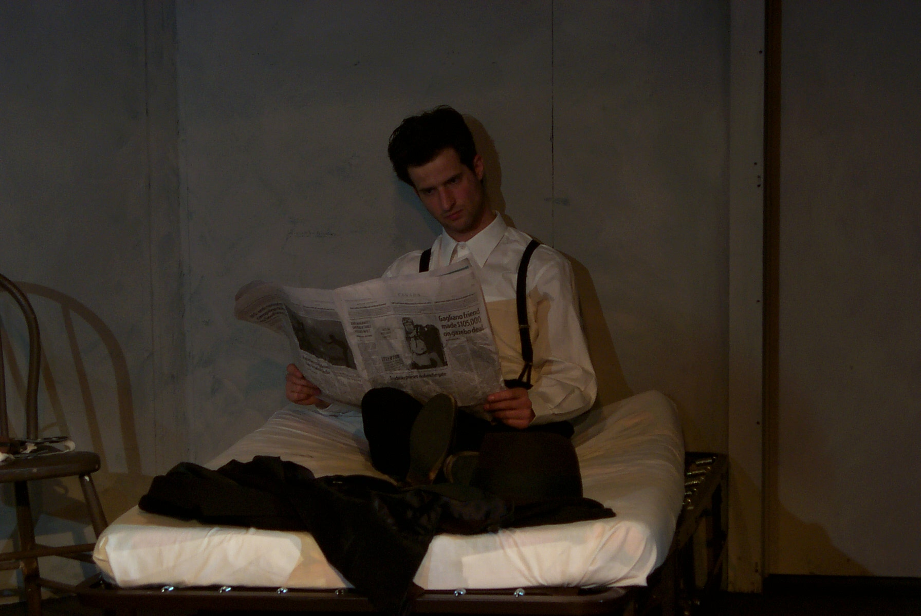 Man sitting on a bed, reading the newspaper