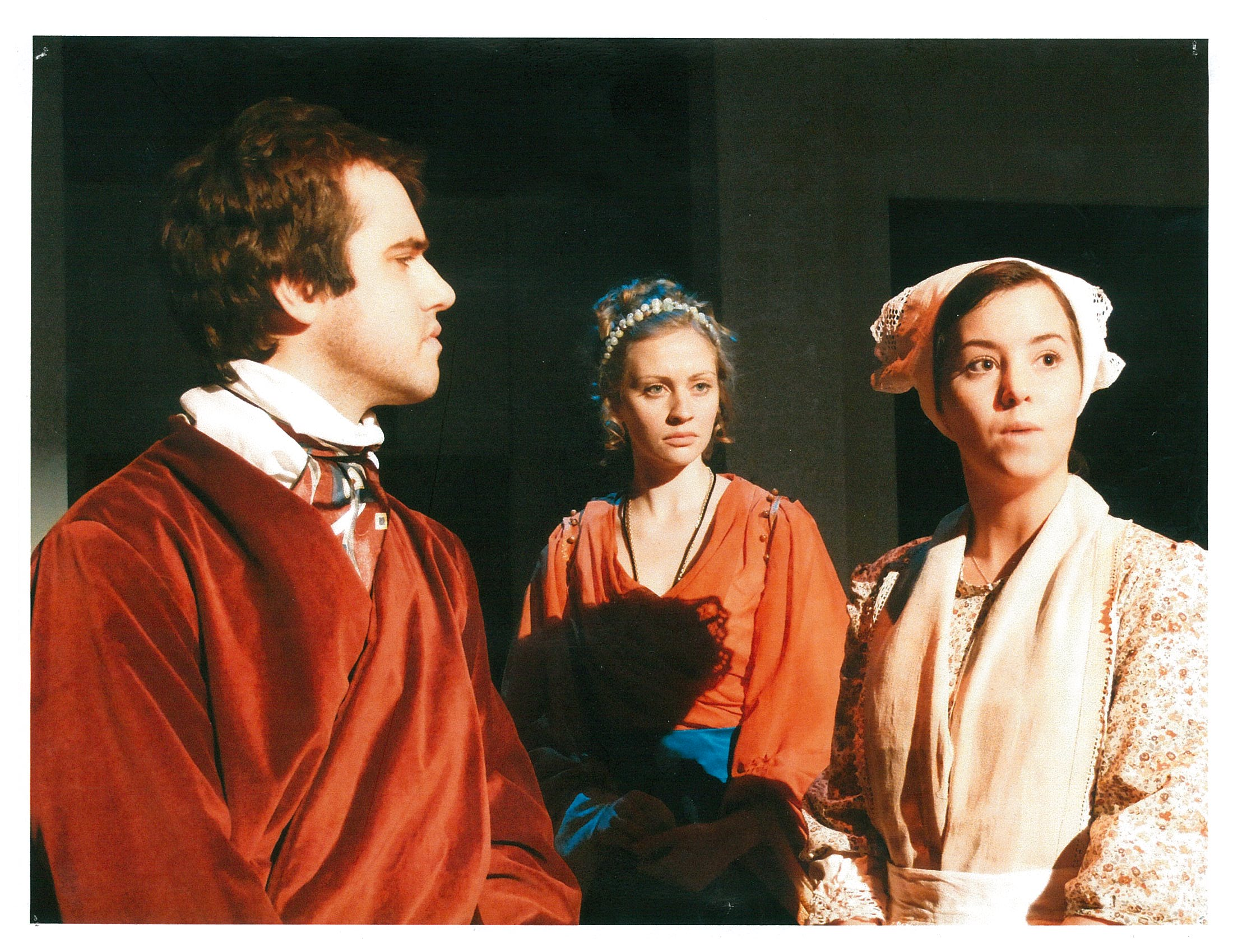 One man in red cloak and two women looking off-screen